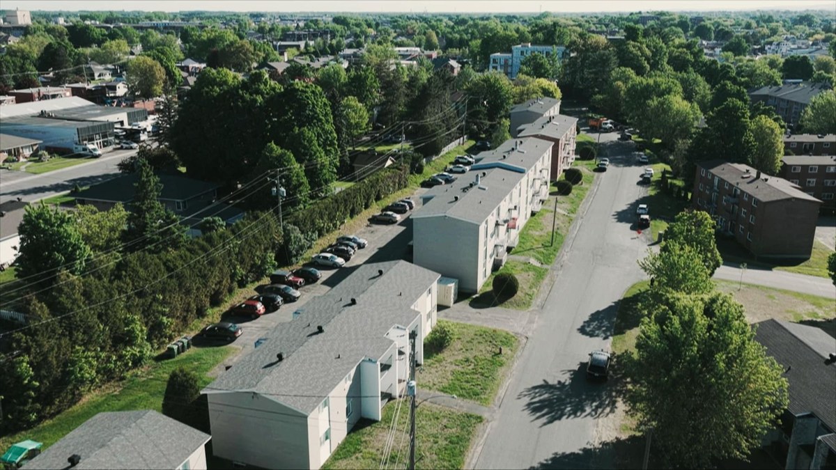 航拍 Victoriaville 一条街边的几栋三层出租公寓楼，楼后是停车场和树林
