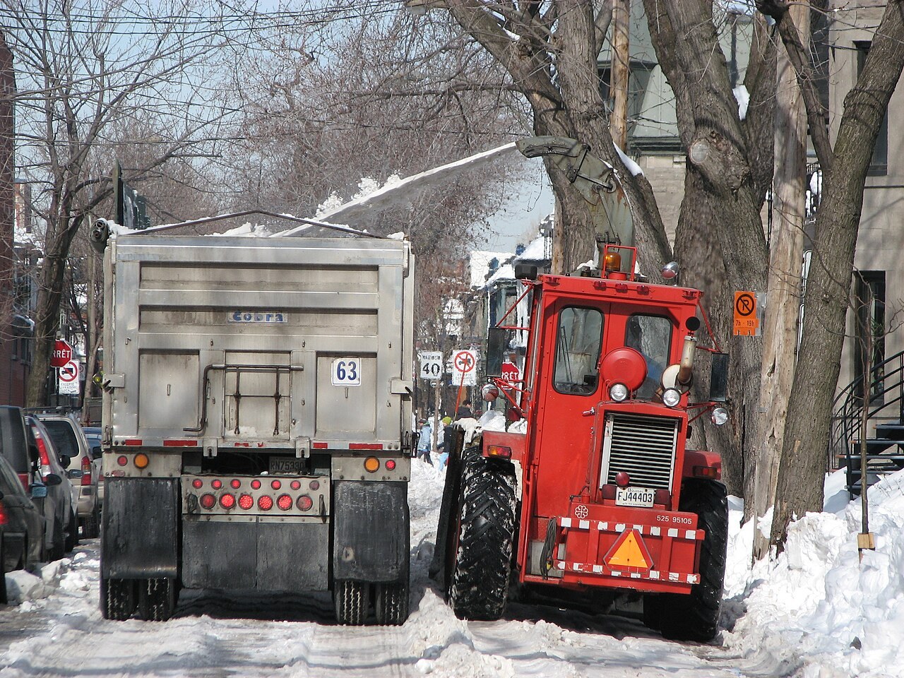 蒙特利尔一条住宅街上，红色装载机把雪吹进旁边的卡车车斗