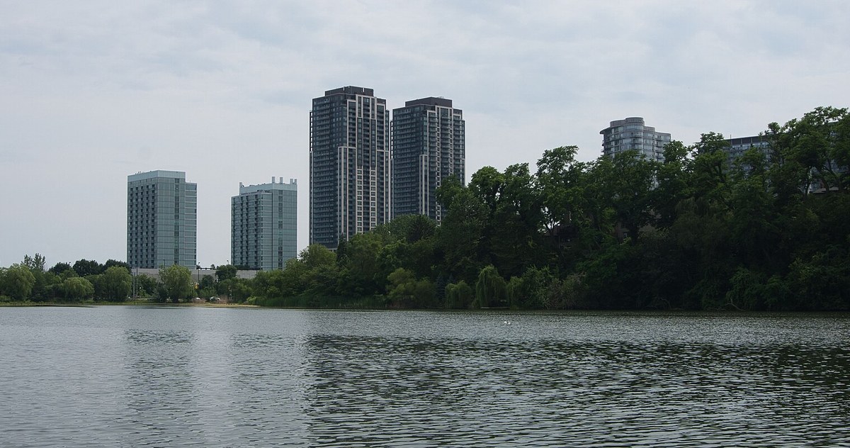 湖对岸树林后面立着几栋高层 condo 公寓楼，天空阴沉